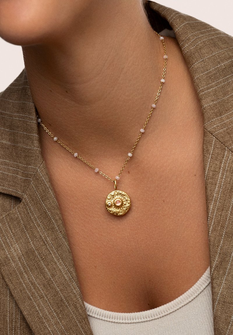 Goldene Anhänger-Halskette mit einem strukturierten runden Charm und Perlen, akzentuiert von kleinen hellrosa Perlen an einer zarten Kette.