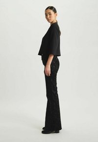 Top noir court associé à un pantalon noir évasé orné de sequins ; texture lisse avec des détails scintillants ; mannequin de profil à droite sur un fond neutre.