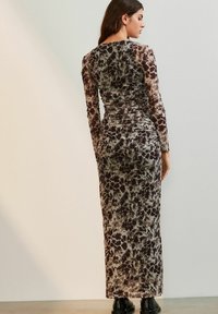 Rochie lungă, ajustată, dintr-un material texturat și transparent, cu un model abstract în nuanțe de maro și gri. Mâneci lungi și design până la podea.