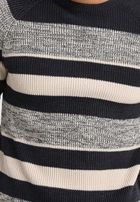 Sweter w paski w odcieniach granatu i beżu z żebrowaną teksturą. Posiada paski o różnej szerokości, z subtelnym melanzowaniem w jaśniejszych obszarach.