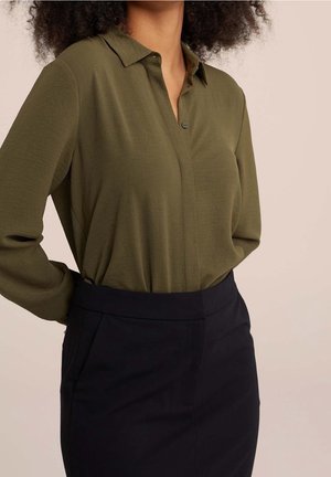 Blouse vert olive à manches longues avec col et patte de boutonnage, associée à une jupe noire taille haute. Tissu lisse et coupe décontractée.