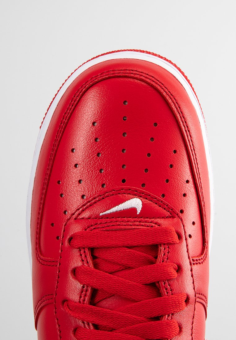 Baskets athlétiques en cuir rouge avec des perforations sur la boîte à orteils, des lacets plats rouges et des accents blancs sur la semelle et le logo.