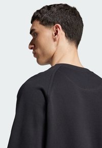 Felpa nera con maniche raglan, realizzata in tessuto strutturato, presenta un collo arrotondato e cuciture a contrasto lungo le spalle.
