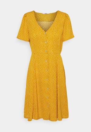 Gelbes Kleid mit kurzen Ärmeln, V-Ausschnitt, weißem herzförmigem Muster und einer durchgehenden Knopfleiste. Der ausgestellte Rock reicht unter das Knie.