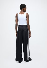 Črne široke hlače z gladko teksturo, z belimi bočnimi črtami in dvema zadnjima žepoma. Kombinirane z oprijetim belim majčnim topom.