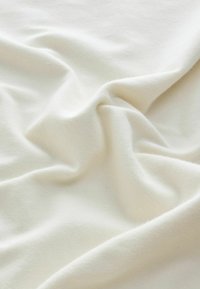 Zacht, off-white stof met zachte plooien en een gladde, licht gestructureerde oppervlakte, getoond van dichtbij.