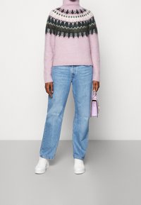 Różowy sweter na drutach z wzorem na karczku, jasnoniebieskie dżinsy i białe trampki. Trzyma małą lawendową torebkę.
