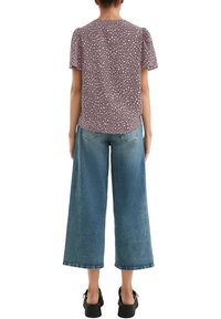 Camicia a maniche corte color mauve con macchie crema, abbinata a jeans in denim blu a gamba larga e scarpe con zeppa nere.