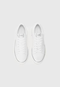 Hvide sneakers med en glat læderfinish, flade snørebånd og diskret branding. Har en sort accent langs sålen og en rund tådesign.