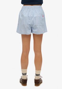 Blå og hvide stribede shorts med elastisk talje, der har en baglomme og rødt logo-detalje. Blødt bomuldsstof, afslappet pasform.