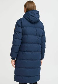 Temno modra puhafna jakna s kapuco, ki ima prešito zasnovo, elastikaste manšete in vidno logotipno nalepko na levem roki.