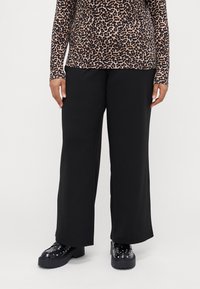 Black wide-leg trousers made of soft fabric, featuring a smooth texture and tailored fit, paired with chunky black shoes with studs.