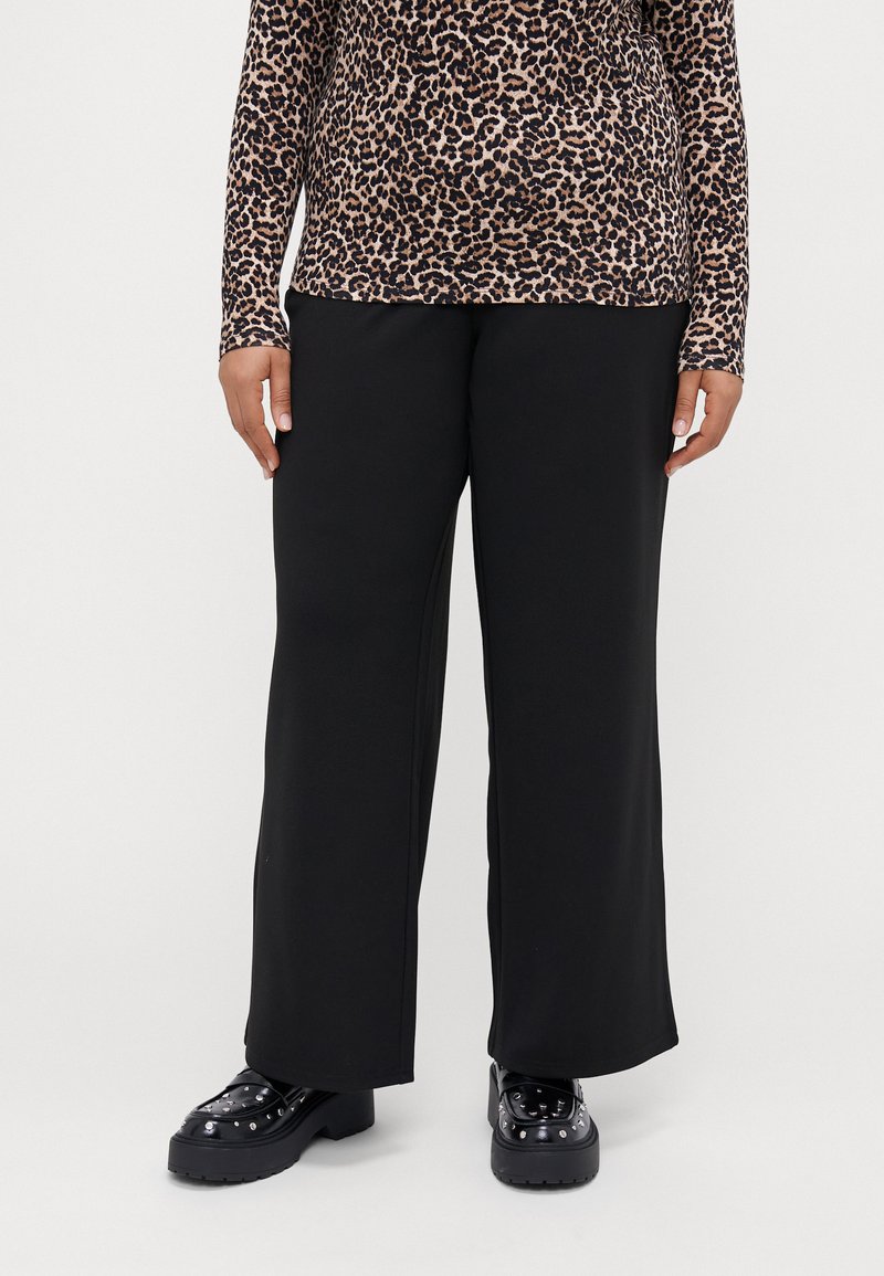 Black wide-leg trousers made of soft fabric, featuring a smooth texture and tailored fit, paired with chunky black shoes with studs.