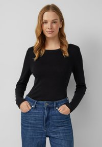 Maglietta nera a maniche lunghe con scollatura tonda, abbinata a jeans in denim blu a vita alta. Il tessuto sembra morbido e aderente.