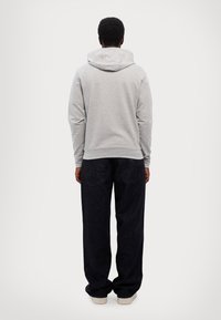 Grå hettegenser med stor hette, ribbede mansjetter og kant, kombinert med mørkeblå brede jeans og hvite sneakers. Rent, enkelt design.