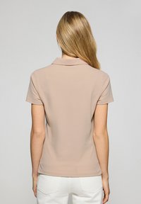 Ljusbeige pikétröja med krage och korta ärmar. Slät tyg med en figurnära design. Bakifrån som visar enkla, rena linjer.