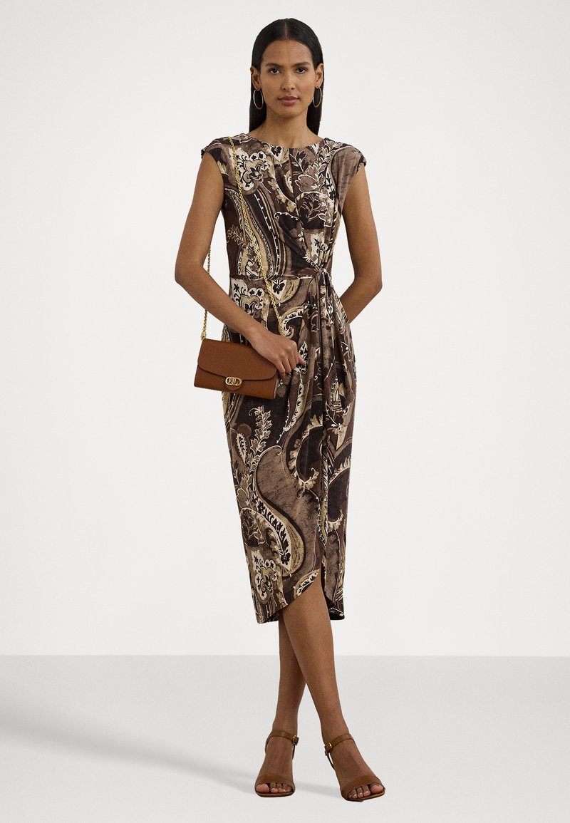 Brązowa sukienka w kwiatowy wzór paisley z krótkimi rękawami, dopasowaną talią i długością do kolan. Uzupełniona o małą brązową torebkę.