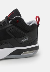 Zapatilla negra que cuenta con materiales de malla y sintéticos, acentos rojos, patrón texturizado, media suela blanca y una unidad de aire visible.