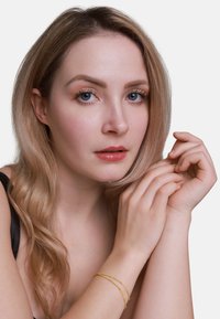 Ingrandimento di una persona con capelli ondulati, castano chiaro, che indossa una maglia nera e un delicato bracciale d'oro a doppio filo al polso.