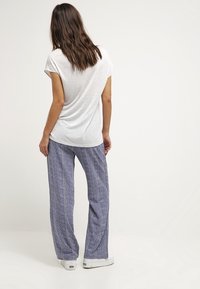 Camiseta gris de manga corta combinada con pantalones anchos de pata ancha de color azul con un diseño de espiga y zapatillas blancas.