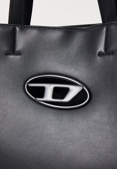 Sac fourre-tout en cuir noir avec une surface texturée, dotée d'un logo ovale argenté brillant en relief comme détail marquant.