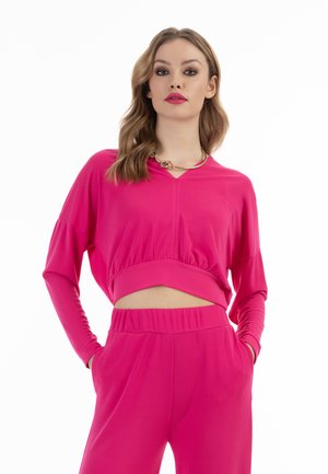 Fuchsia cropped sweatshirts med lange ærmer, ribbet kant og V-hals; parret med matchende høj taljede bukser med elastisk talje.