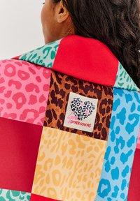 Mnohofarebný patchwork šál s leopardími vzormi v ružovej, zelenej, hnedej, žltej a modrej farbe. Obsahuje značkovú nálepku s dizajnom srdca.