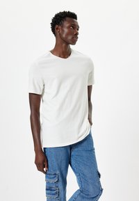 Witte t-shirt met korte mouwen en een subtiele v-hals, gemaakt van een zachte katoenen stofmix, gecombineerd met blauwe cargobroek met zijzakken.
