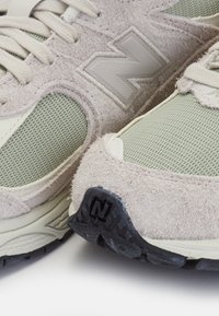 Obuv vyrobená z světle hnědého semiše s sieťovými detaily v jemně zelené barvě, s černou gumovou podrážkou, na které je zvýrazněno logo.