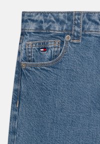 Denim jeans in light blue, featuring a front pocket with a small red, white, and blue logo, and contrasting stitching. Textured fabric finish.