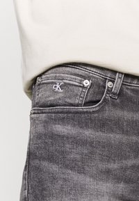 Los jeans de mezclilla gris cuentan con un lavado sutil, dos bolsillos frontales, un pequeño logo bordado de 'cK' y detalles en plata en la cintura.