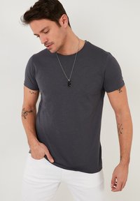 Sötét szürke, rövid ujjú póló puha, sima anyagból. Kerek nyakú, laza szabású, fehér nadrággal párosítva. Minimalista dizájn, minta nélkül.