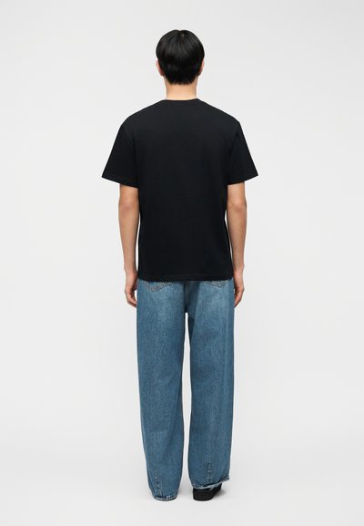 Μαύρο βαμβακερό t-shirt με κοντά μανίκια, συνδυασμένο με ανοιχτό μπλε τζιν παντελόνι με ευρύ πόδι, πίσω τσέπες και άνετη εφαρμογή. Απλός σχεδιασμός.