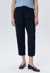 Pantalon bleu marine, léger, à taille élastique avec une coupe décontractée et des ourlets roulés, associé à des chaussures noires à enfiler à semelle plate.