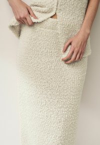 Ensemble en tricot à deux pièces en blanc cassé, présentant une surface texturée avec une coupe ample, une fente sur le côté et un détail de poche plaquée.
