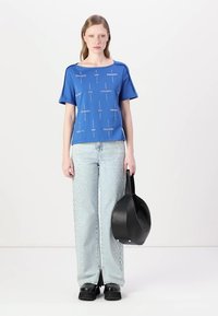 Top azul de manga corta con texto estampado, combinado con unos jeans de pierna ancha en azul claro con acentos metálicos y un bolso negro. Zapatos negros gruesos.