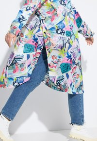 Multicolore, lichtgewicht shirtjurk met grafische prints van mariene levens en strandscènes, gecombineerd met blauwe denim jeans en witte chunky laarzen.