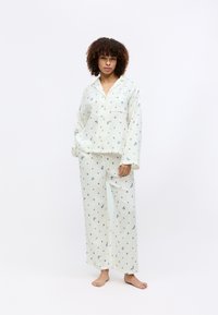 Biała piżama w niebieskie kwiatowe wzory. Luźna, zapinana na guziki bluzka z kieszonką, w zestawie z szerokimi spodniami. Wykonana z strukturalnego materiału.