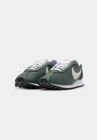 Zöld textil és velúr sportcipők fehér fűzővel, bézs swoosh logóval és fekete gumitalppal. Alacsony profilú kialakítással rendelkezik.