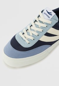 Blå kanvas sneakers med kremfargede snørebånd og detaljer. Har en teksturert gummisåle og en logomerketag på tungen. Designet med lagdelte fargeblokker.