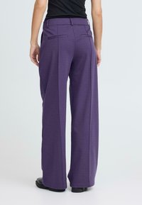 Pantalons larges en tissu violet avec une texture lisse, comportant des poches arrière et une taille ajustée. Design uni, sans motifs visibles.