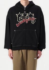 Sweat à capuche noir avec fermeture éclair, orné d'un grand motif texte en crème et bordeaux, avec poches avant et surpiqûres blanches contrastantes.