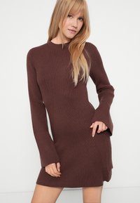 Pruun soonikkoeslineeritud kleit, pikkade varrukatega ja kõrge kaelusega. Omaduseks on keha järgiv lõige ja peened diagonaalsed mustriga detailid.