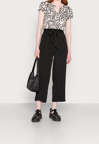 Femme portant un pantalon noir taille haute à jambes larges et court avec ceinture nouée, un haut à manches courtes à imprimé zèbre, un sac à main noir et des sandales plateformes noires.
