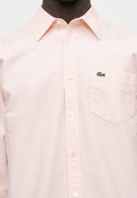 Chemise pour homme rose clair à rayures avec col et poche poitrine arborant un logo crocodile vert.
