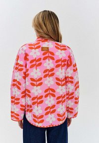Prešívaná bunda z ružovej látky s veľkým červeným a bielym kvetinovým vzorom, s golierom, zakriveným lemom a logom pri krku.