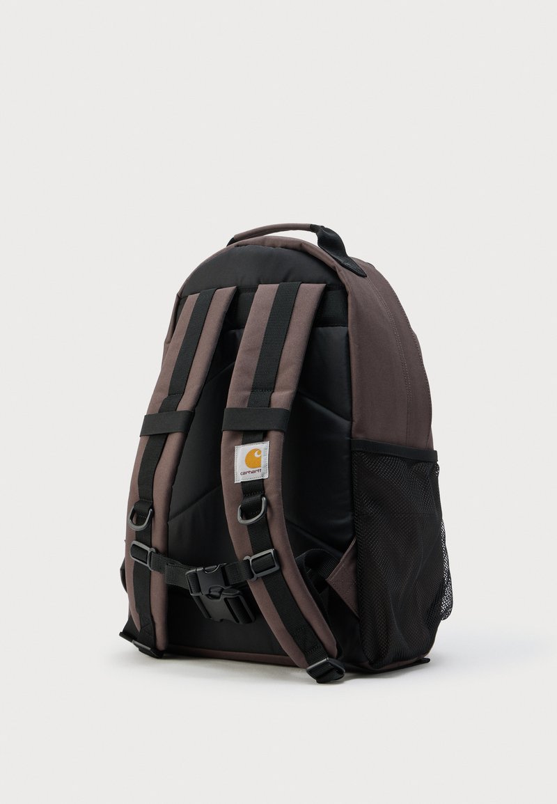 Donkerbruine en zwarte rugzak met gevoerde banden, borstsluiting, Carhartt-logo en een gaasvak aan de zijkant op een witte achtergrond.