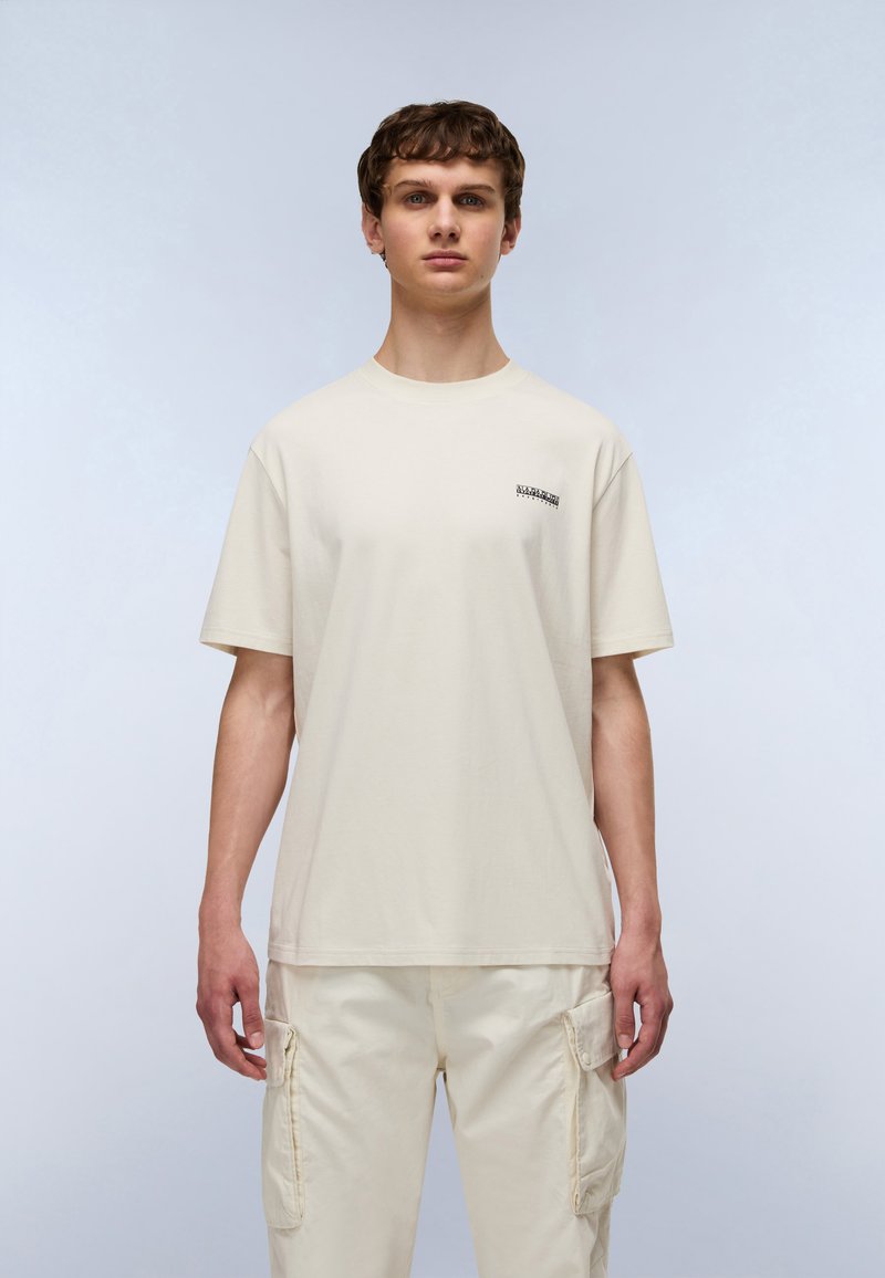 Μπεζ βαμβακερό μπλουζάκι με στρογγυλή λαιμόκοψη και κοντά μανίκια. Διαθέτει μικρό γραφικό στην περιοχή του στήθους, με άνετη εφαρμογή.