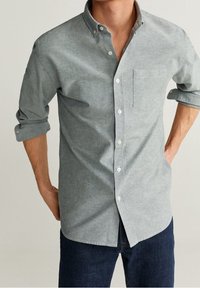 Camisa gris de botones hecha de tejido ligero, con un solo bolsillo en el pecho, mangas enrolladas y detalles en botón blanco.