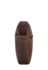 Brūna ādas soma ar vertikālu dizainu, ar teksturētu sānu, izturīgu auduma siksnu un ar rāvējslēdzēju. Kompakta un plāna forma.
